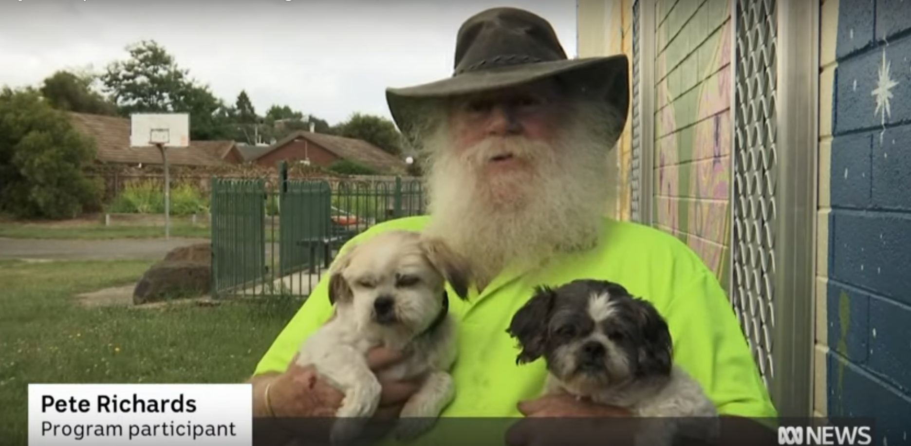 A man in a neon yellow shirt holding two dogs, one blond and one brown.